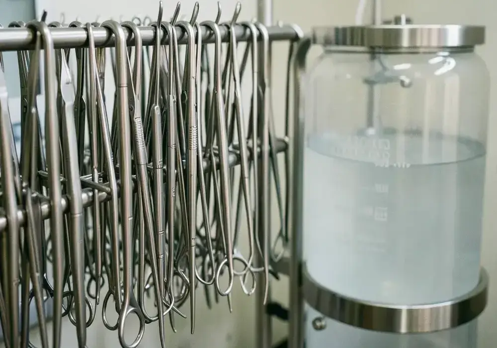 Polished stainless steel surgical instruments on a passivation rack beside a rinse tank