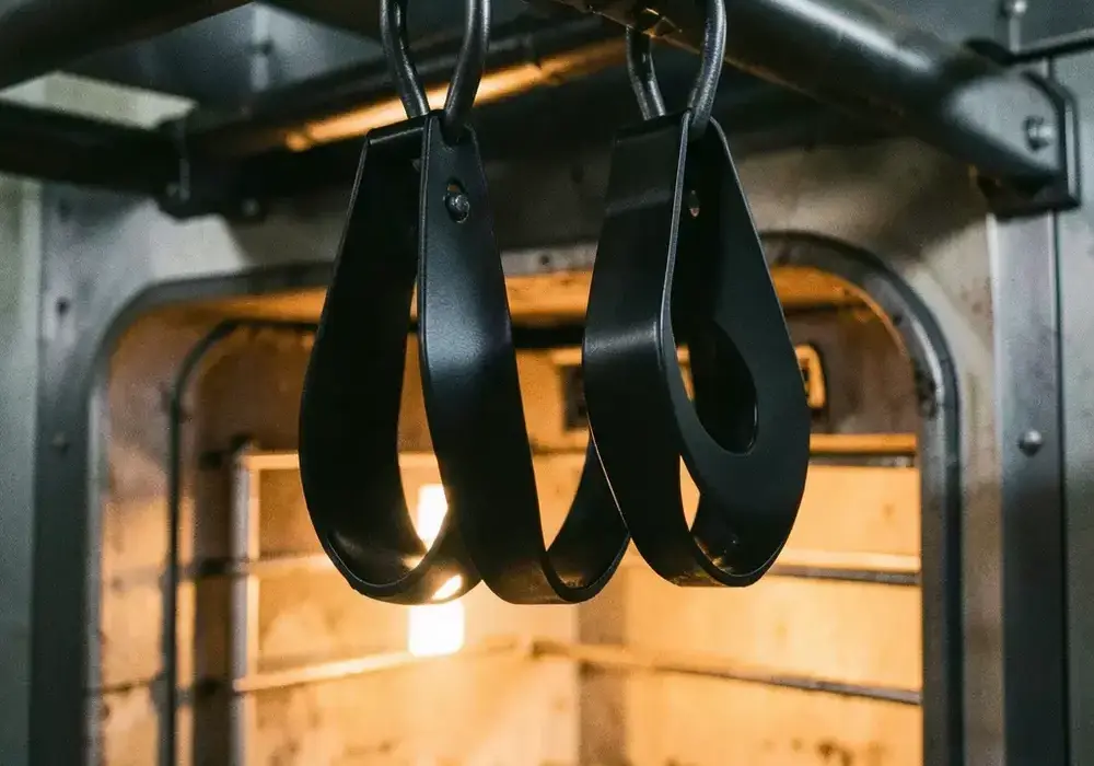 Powder coated parts hanging from an overhead conveyor entering a curing oven
